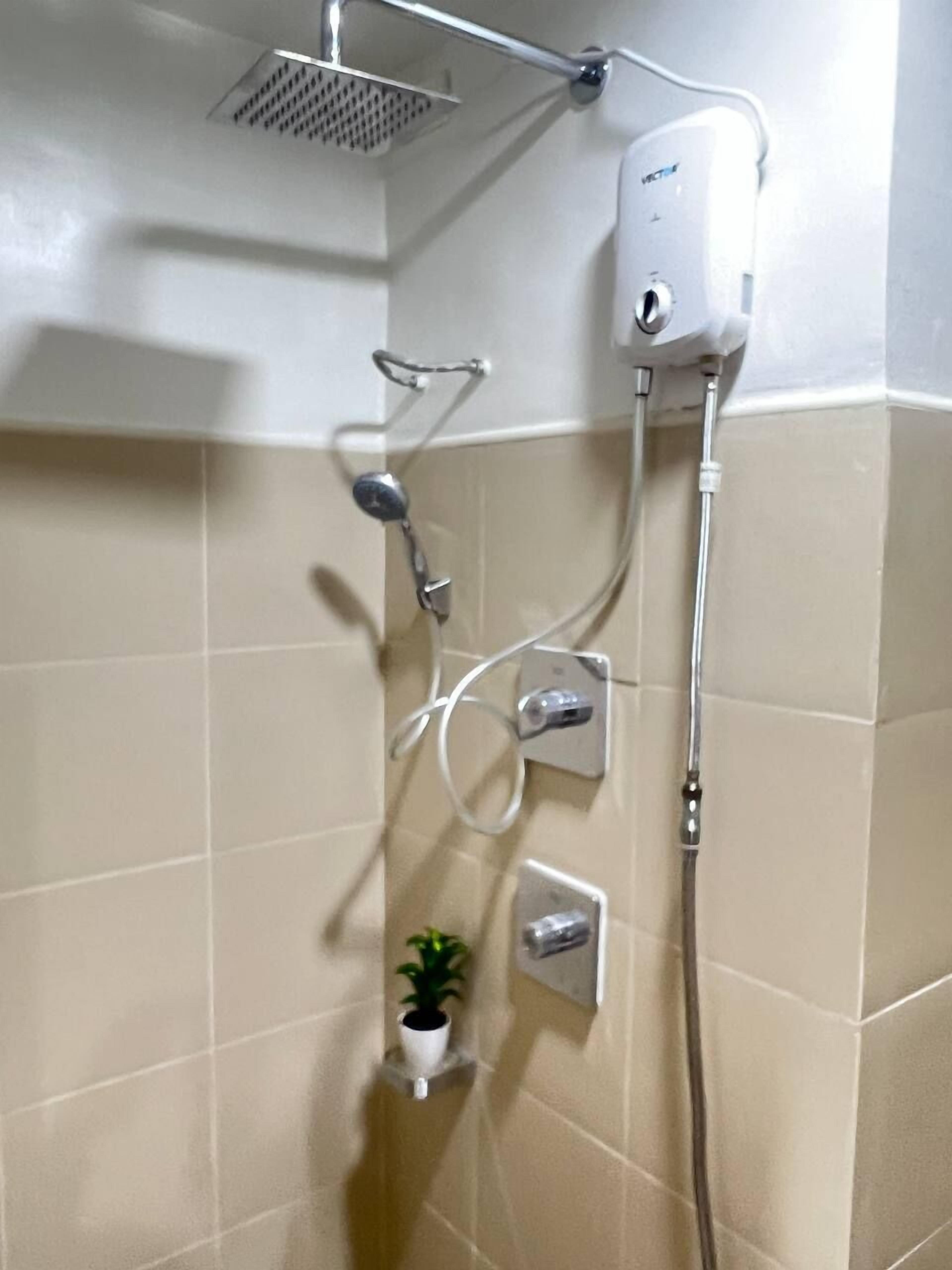 Ein Badezimmer mit Dusche, Duschkopf, einer fest installierten Bedienfeld und einem kleinen Topfpflanz auf einem Regal.
