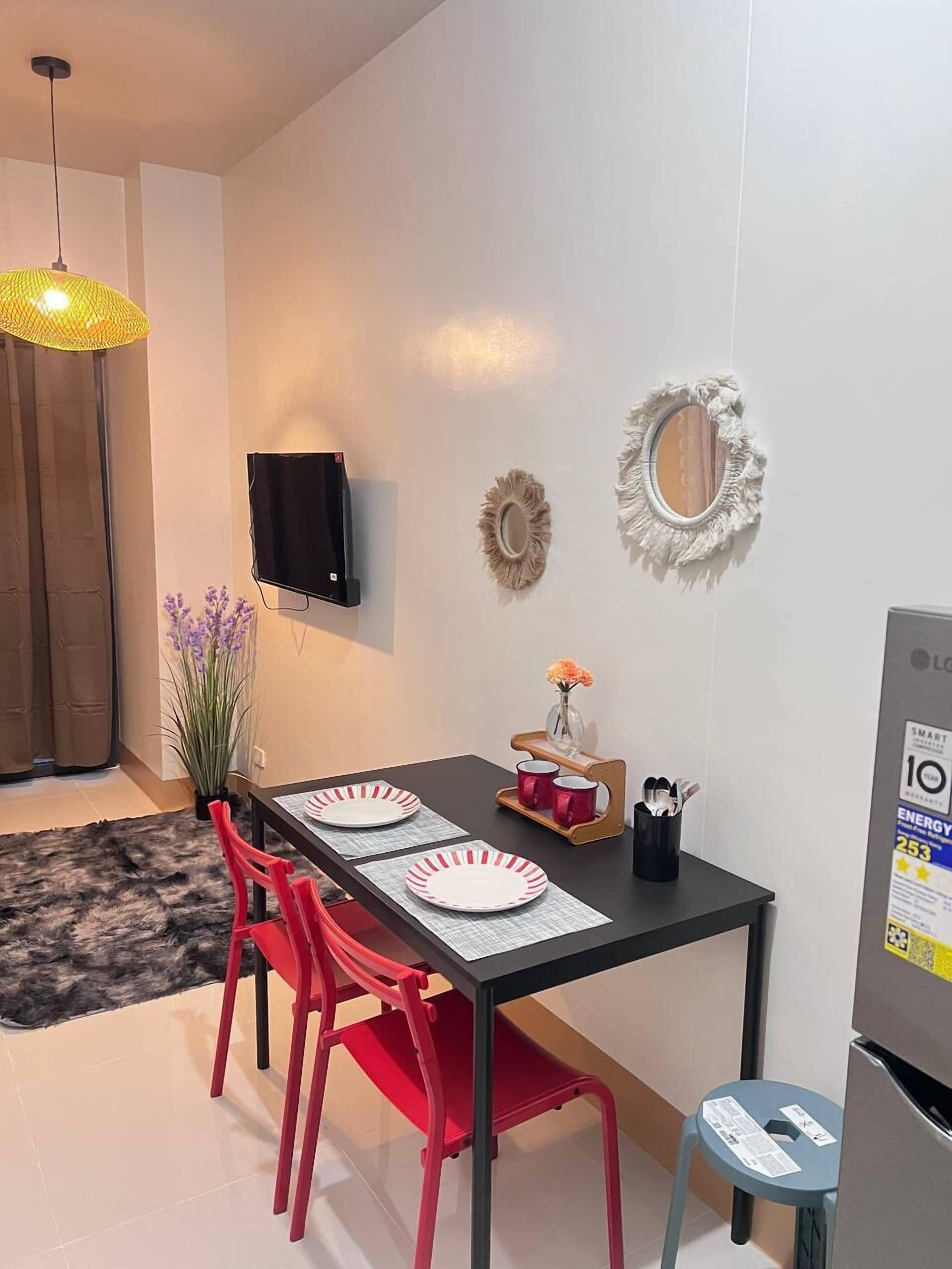 Ein moderner Essbereich mit einem schwarzen Tisch, roten Stühlen und einem kleinen Hocker. Ein Fernseher ist an der Wand montiert, und es befinden sich dekorative Wandbilder dort.