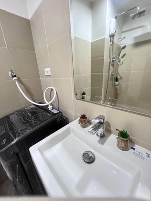 Un baño con lavamanos blanco, espejo, ducha y encimera de mármol negro.