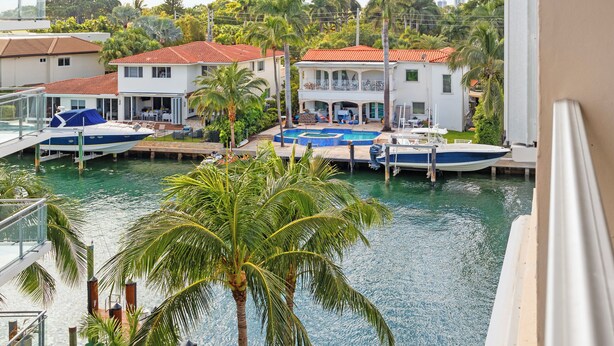 A balcony with a view of a marina, boats docked, and a building with a red roof. - Bay Harbor Sunset Apt 5B (Bay Harbor Islands)