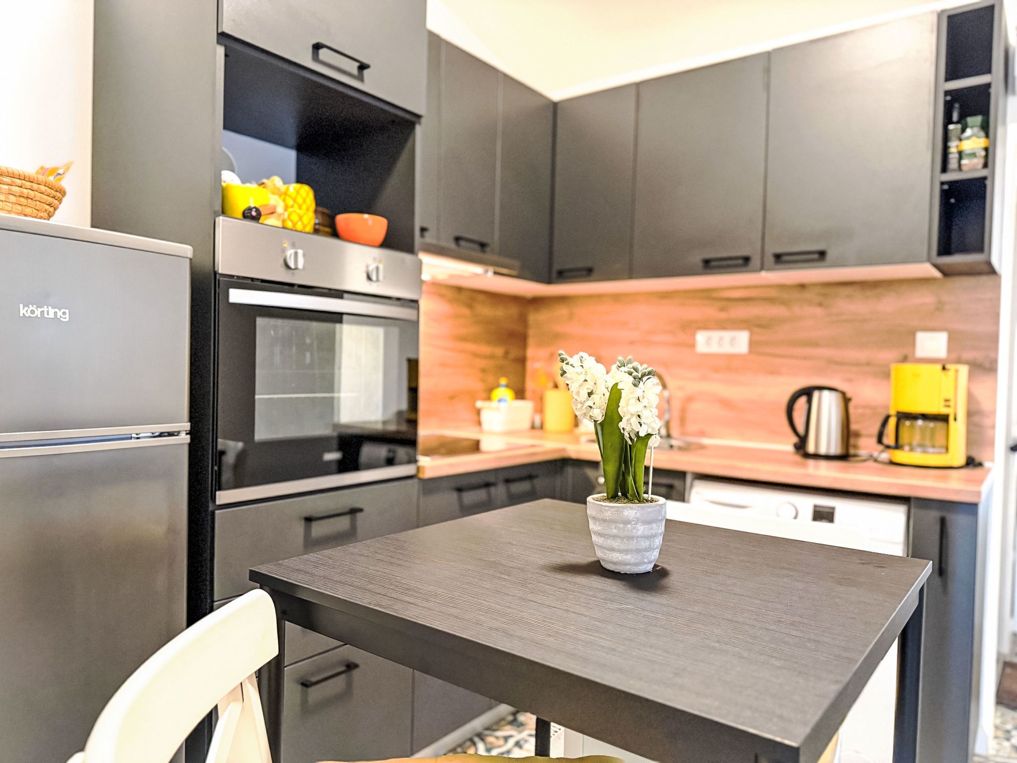 A modern kitchen with grey cabinets, a stainless steel refrigerator, an oven, and a coffee machine.