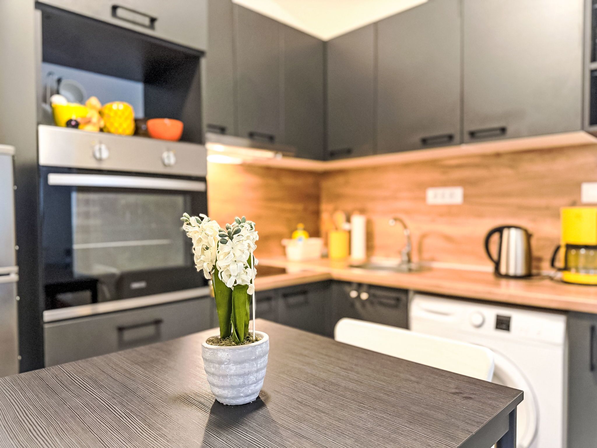 Eine moderne Küche mit dunklen Schränken, einer Holzarbeitsplatte und einem Tisch mit Blumen in einer Vase.