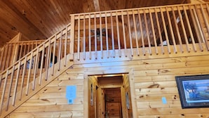 A wooden cabin interior with a staircase leading to a loft area, a dining table, and a sofa. - Cozy 2-bedroom cabin in welcoming lake Douglas, Sevierville near Pigeon Forge (Sevierville)