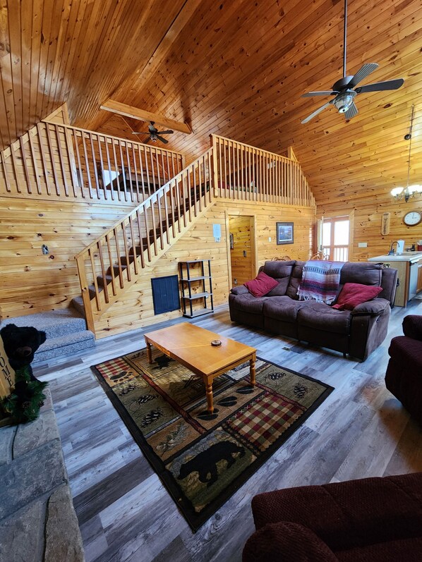 A wooden cabin interior with a staircase, a sofa, a coffee table, and a ceiling fan.