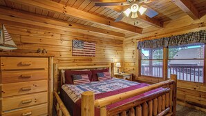 A wooden cabin bedroom with a bed, a dresser, a ceiling fan, and a window with a view of the outside. - Cozy 2-bedroom cabin in welcoming lake Douglas, Sevierville near Pigeon Forge (Sevierville)