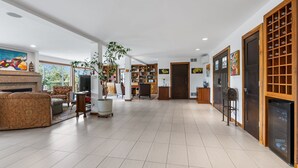 Ein geräumiges Wohnzimmer mit Kamin, einer großen Couch und einem Couchtisch. Im Hintergrund sind Holzregale und ein Essbereich zu sehen.