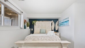 A bedroom with a bed, a nightstand, a dresser, a window, a wall-mounted shelf with plants, and a painting. - Charming 2-bedroom condo central NW (Calgary)