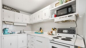 A modern kitchen with white cabinets, a built-in microwave, a stove, and a coffee maker. - Charming 2-bedroom condo central NW (Calgary)