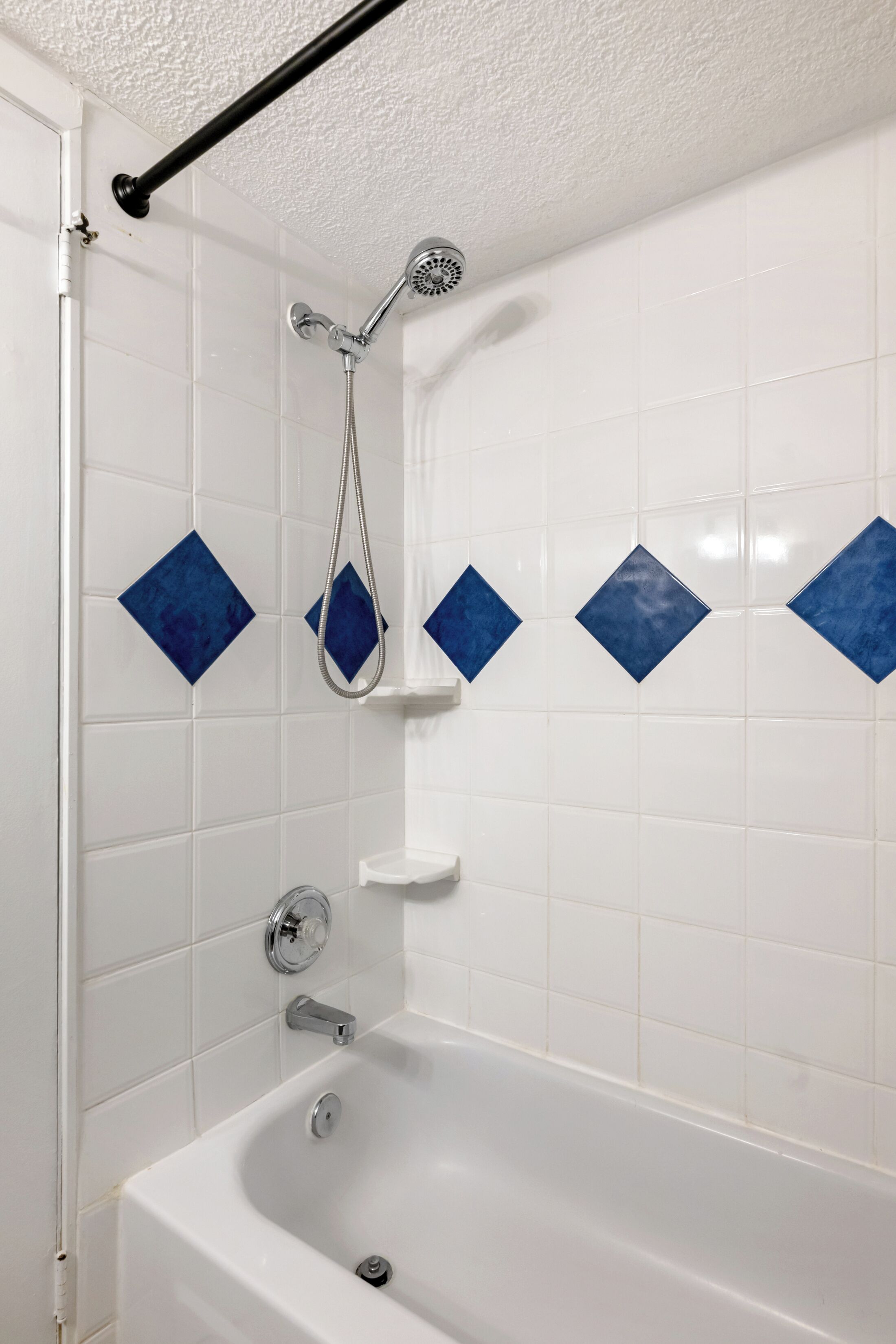 A bathroom with a white bathtub, a showerhead, and blue diamond-shaped tiles on the wall.