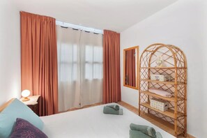 Ein Schlafzimmer mit einem Bett, einem Nachttisch mit Lampe, einem Kleiderschrank und einem Korbregal.