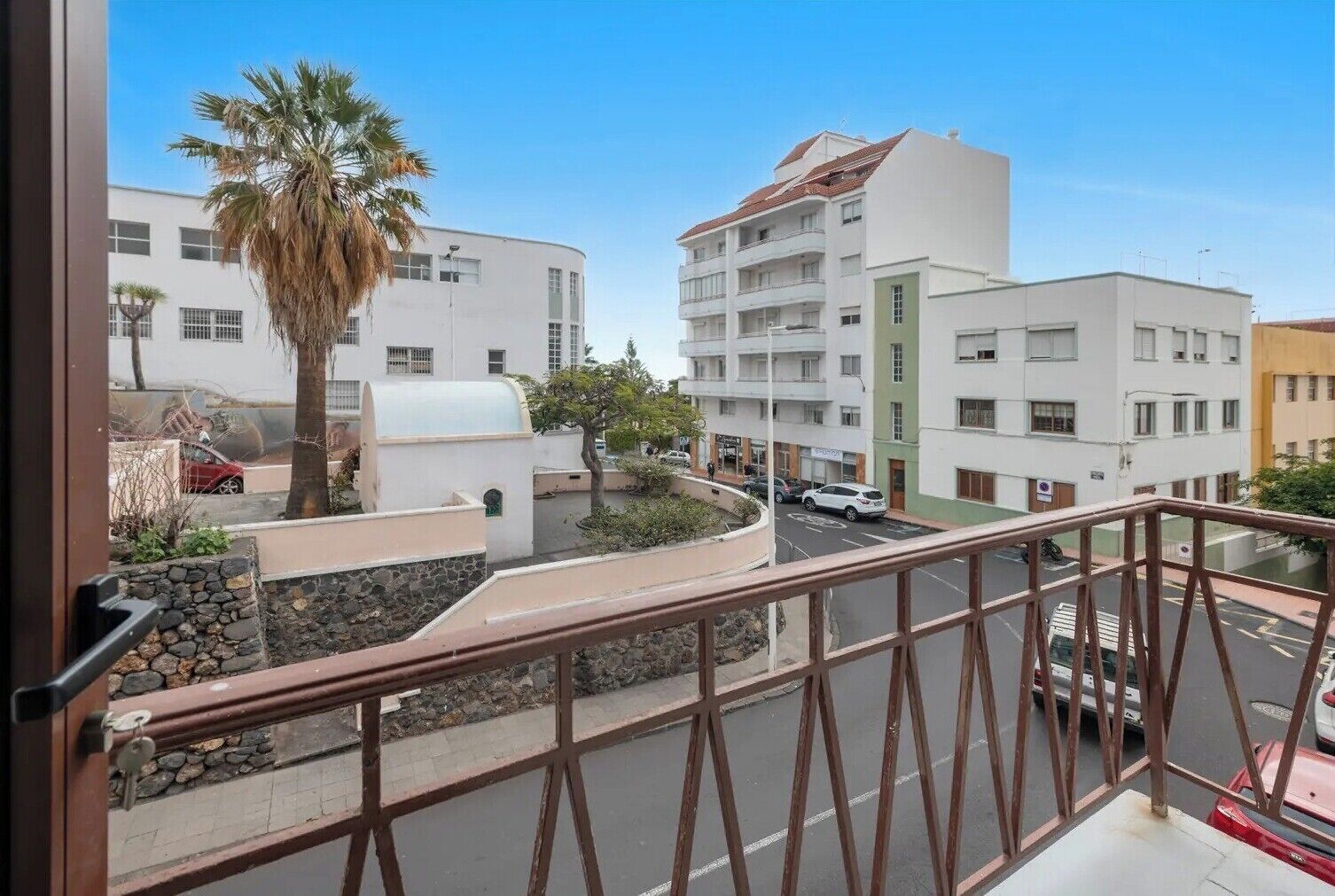 Ein Balkon mit Steinmauer, einer Palme und Blick auf ein mehrstöckiges Gebäude mit Balkonen.