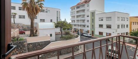 A balcony with a stone wall, a palm tree, and a view of a multi-story building with balconies.