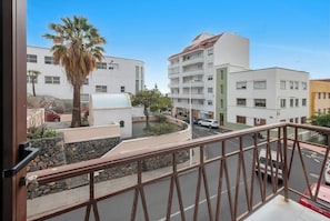A balcony with a stone wall, a palm tree, and a view of a multi-story building with balconies.