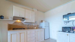 A kitchen with white cabinets, a stove, a sink, and a refrigerator. - Three-room apartment 4 minutes walk from the beach (Olbia)