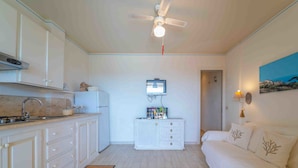 A compact room with a kitchenette, a ceiling fan, a flat-screen TV, a bed with decorative pillows, and a painting on the wall. - Three-room apartment 4 minutes walk from the beach (Olbia)