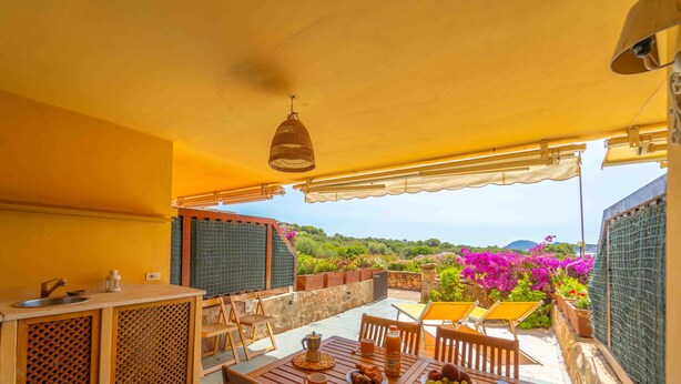 A covered outdoor area with a dining table, chairs, and a hanging light fixture. - Three-room apartment 4 minutes walk from the beach (Olbia)