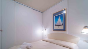 A hotel room with a bed, a framed picture of a sailboat, and two wall-mounted lights. - Three-room apartment 4 minutes walk from the beach (Olbia)
