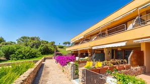 A two-story building with a balcony, stone pathway, and vibrant purple flowers. - Three-room apartment 4 minutes walk from the beach (Olbia)