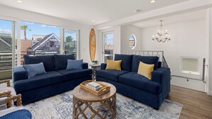 A modern living room with a dark blue sofa set, a round wooden coffee table, and a view of a building outside. - Single Family Retreat | Steps to Bay & Beach | Fireworks Views (San Diego)