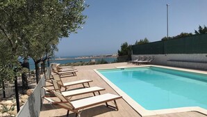Un espace piscine avec des chaises longues et vue sur la mer.