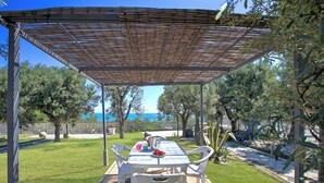Un espace extérieur abrité, aménagé pour les repas, avec une table et des chaises, entouré d’une pelouse bien entretenue et d’arbres.