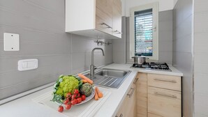 Une cuisine moderne avec des carreaux gris, un évier en acier inoxydable, une cuisinière à gaz et une fenêtre avec des stores.