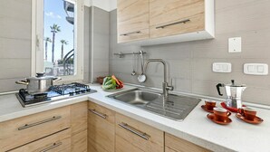 Une cuisine équipée d’une cuisinière à gaz, d’un évier, de placards et d’une fenêtre donnant sur des palmiers.