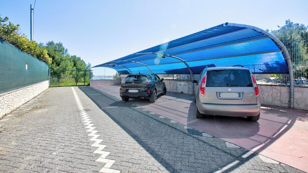 Un área de estacionamiento techada con dos coches aparcados bajo un toldo azul.