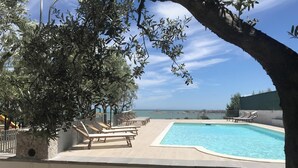 Ein Poolbereich mit Liegestühlen, einem Steinpflanzgefäß und Blick aufs Meer.