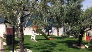 Ein gepflegter Garten mit einem grünen Rasen, einem Spielplatz mit einer Rutsche und einigen Bäumen.