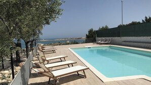 Zona de piscina con sillones de descanso y vista al mar.