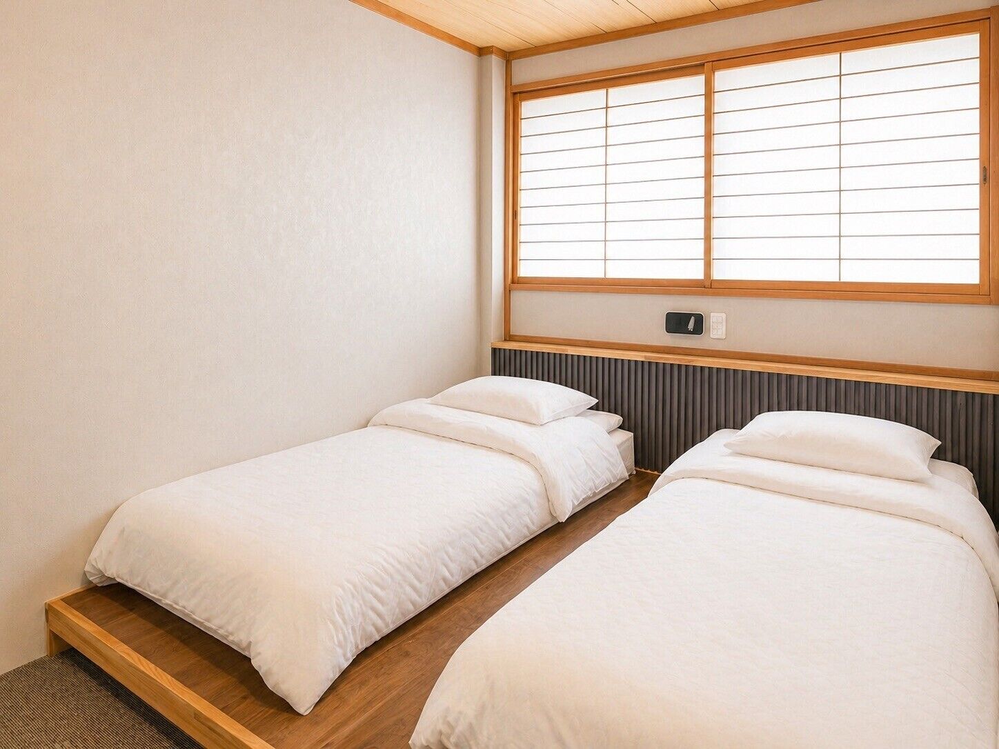 A small, clean room with two single beds, a window with wooden frames, and a radiator below the window.