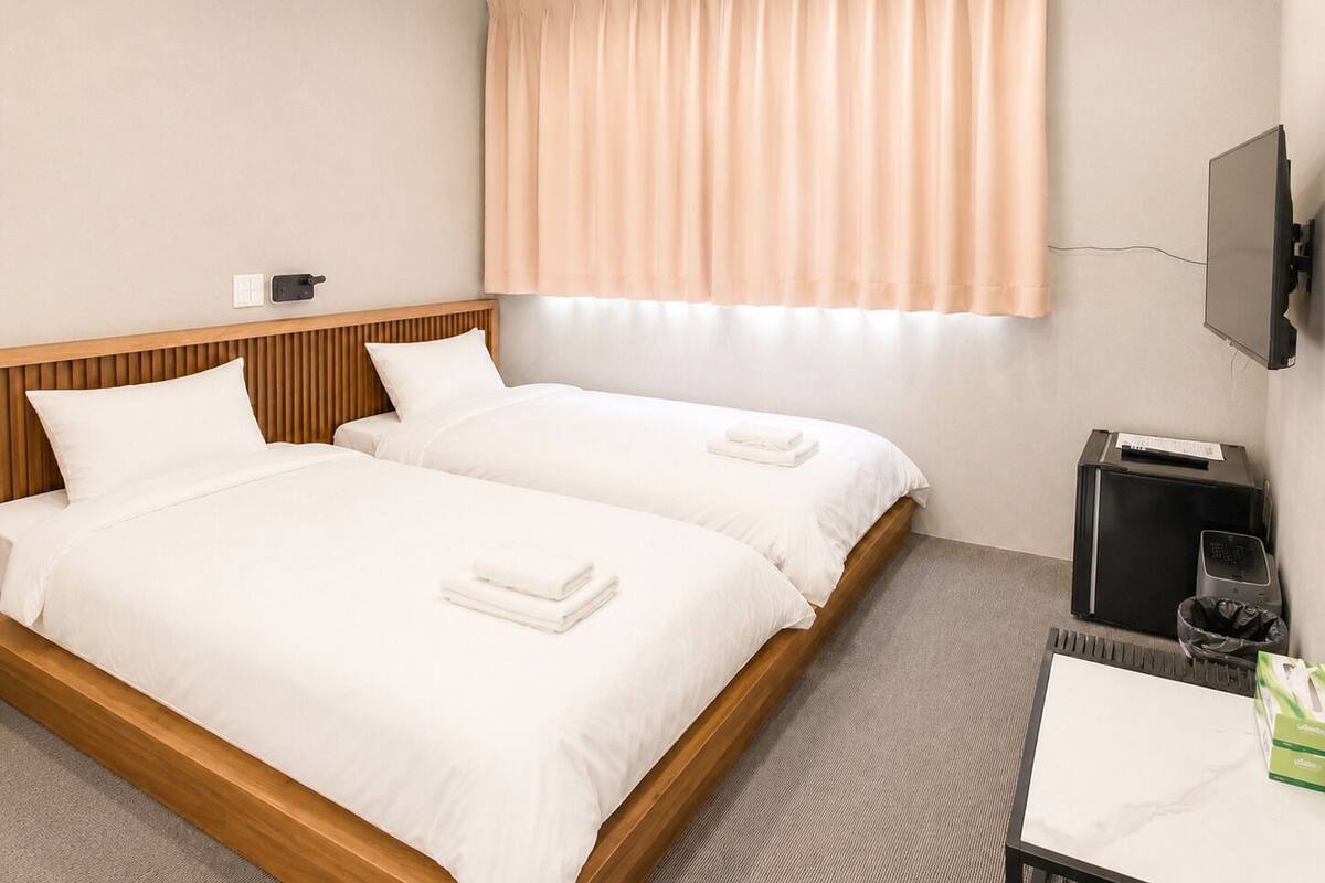 A hotel room with two beds, a TV, a desk, and a window with curtains.