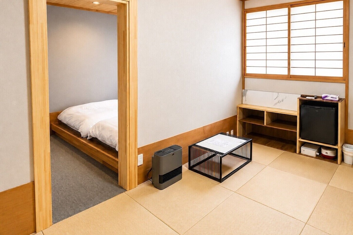 A room with a bed, a small table, a heater, a window with shoji screens, and a wooden cabinet.