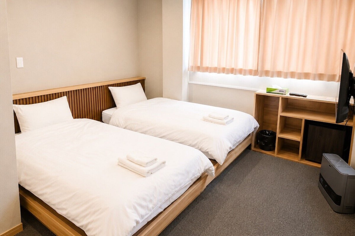 A hotel room with two beds, a TV, a desk, and a window with curtains.
