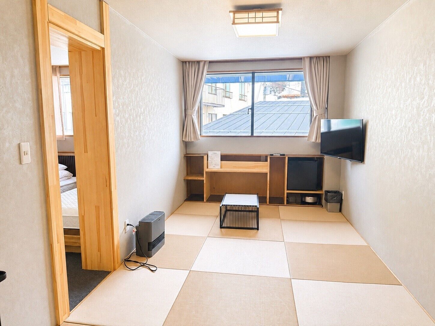 A compact room with a bed, a TV, a desk, and a window with curtains.