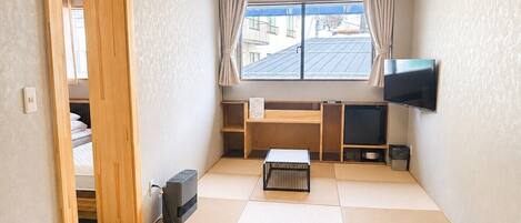 A compact room with a bed, a TV, a desk, and a window with curtains.
