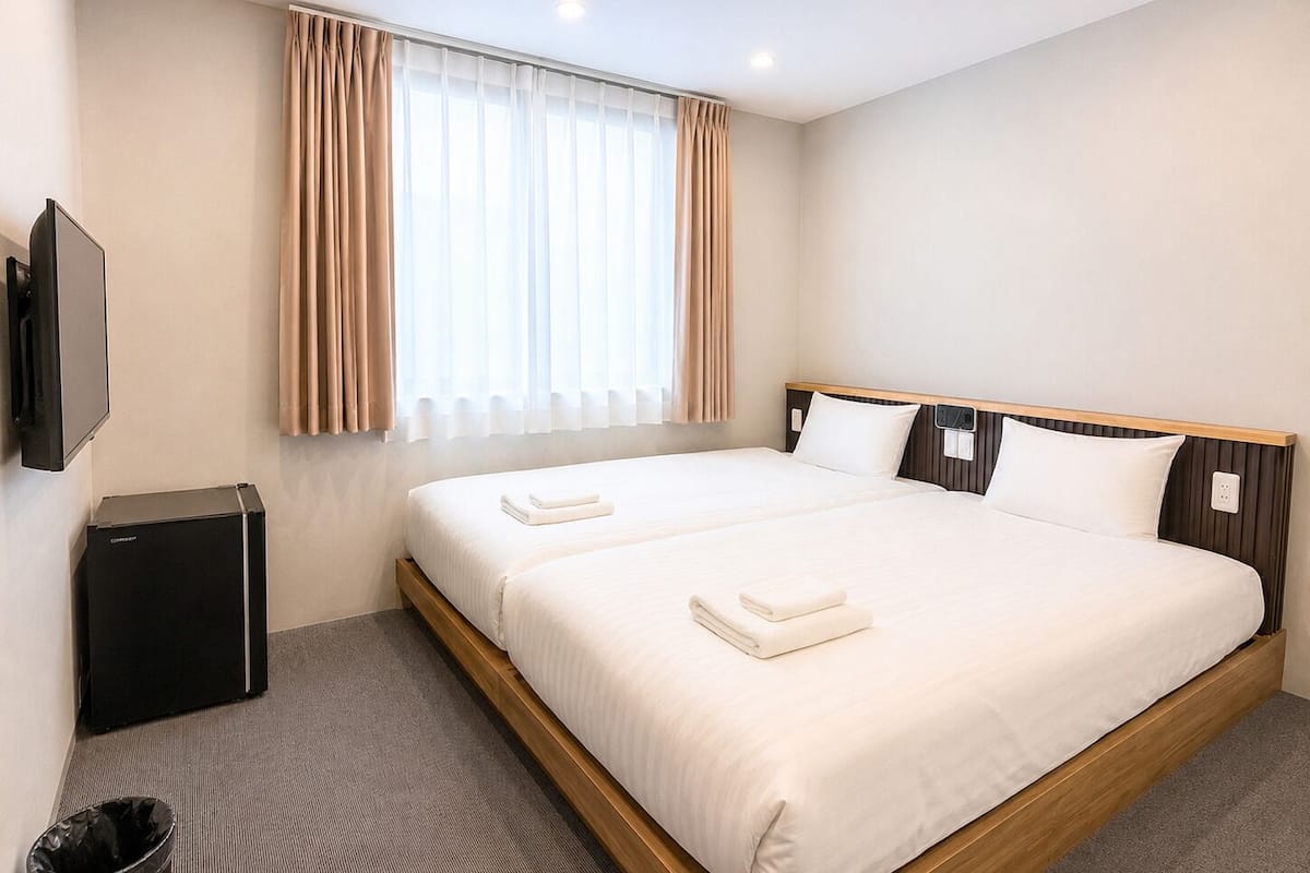A hotel room with a bed, a TV, a trash bin, and a window with curtains.