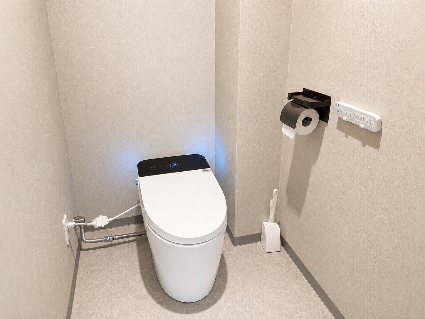 A modern toilet with a digital display, a paper towel holder, and a power outlet on the wall.