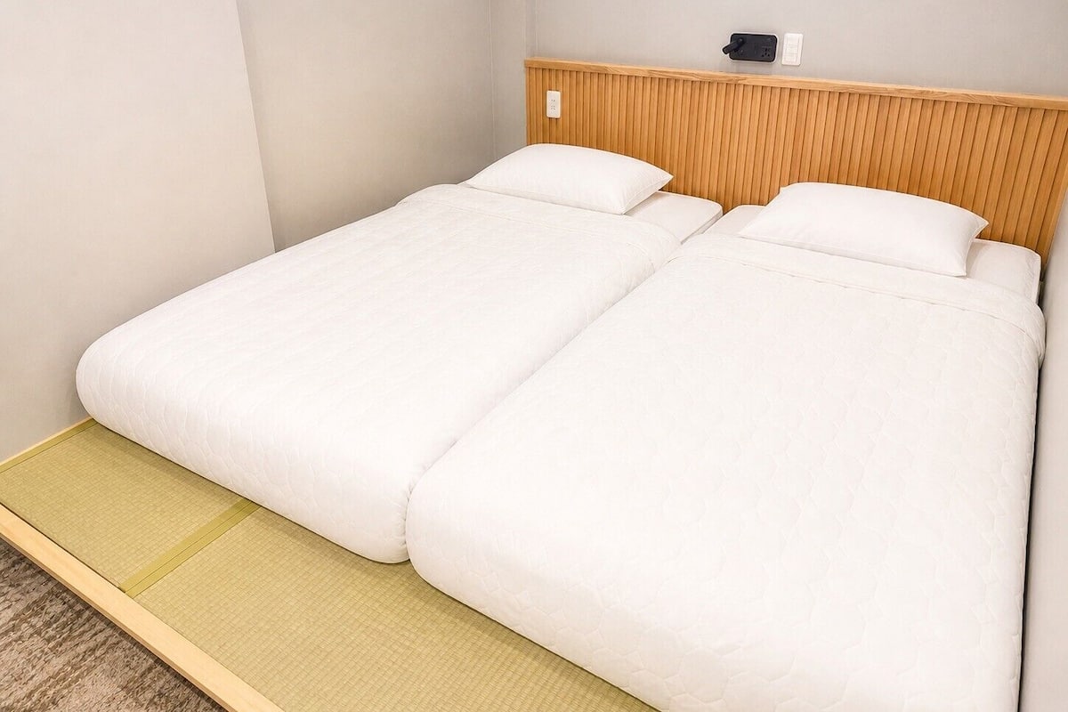A single bed with a wooden headboard, a small bedside table, and a wall-mounted phone.