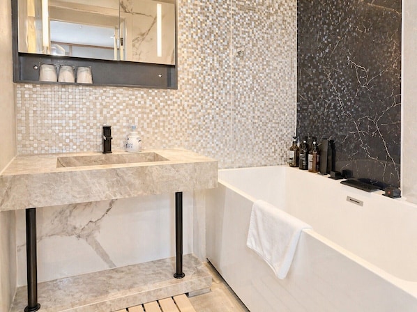 A bathroom with a marble sink, a large mirror, a tiled wall, and a black marble bathtub. - ZaoSunvalley Hotel (Yamagata)