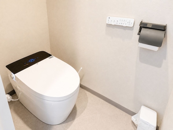 A white toilet with a control panel, a wall-mounted paper dispenser, and a small trash bin. - ZaoSunvalley Hotel (Yamagata)