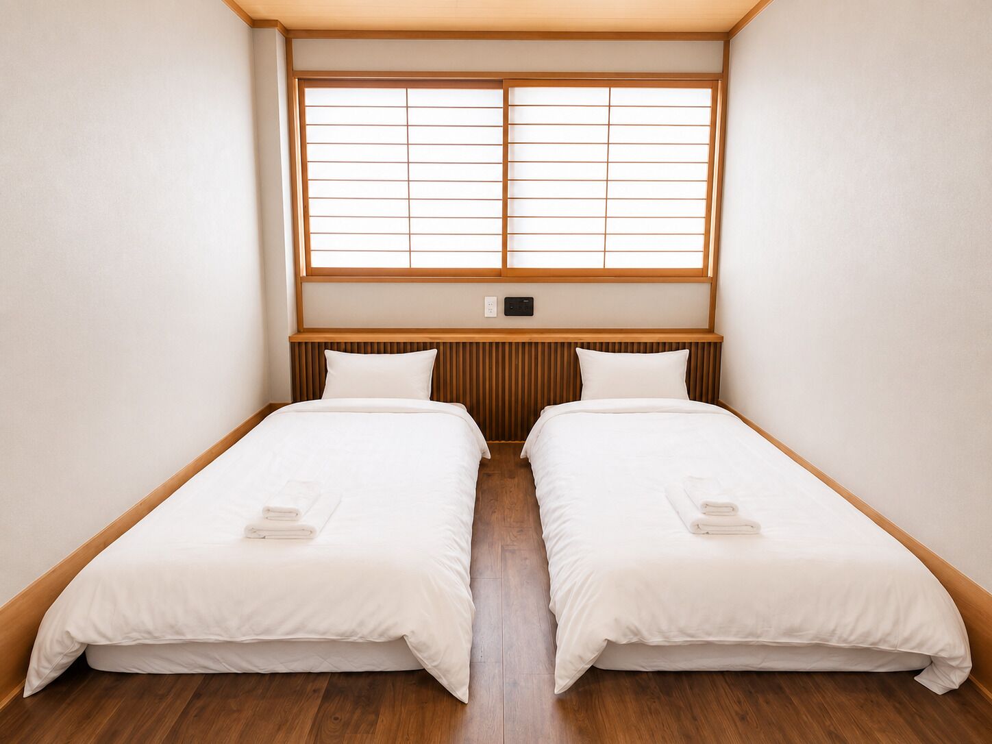 Una habitación con dos camas individuales, cabecero de madera, una ventana con persianas y un interruptor en la pared.