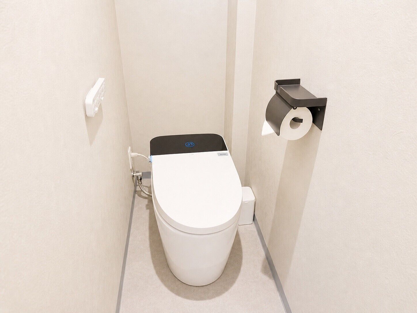 Un inodoro compacto y moderno con accionador de descarga en la pared y dispensador de papel higiénico.