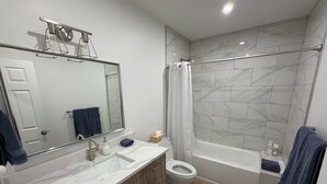Et moderne badeværelse med en marmorvask, træskabe, et toilet og et badekar.