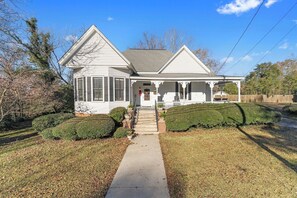 Una casa de dos pisos con un porche delantero, un vestíbulo cubierto y un patio frontal visible con un sendero que lleva a la puerta.