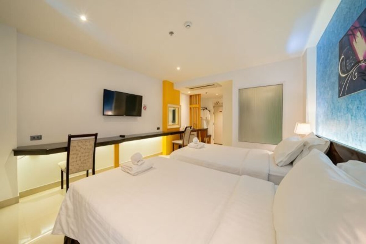 A hotel room with two beds, a TV, a desk with a chair, and a bathroom visible through an open door.