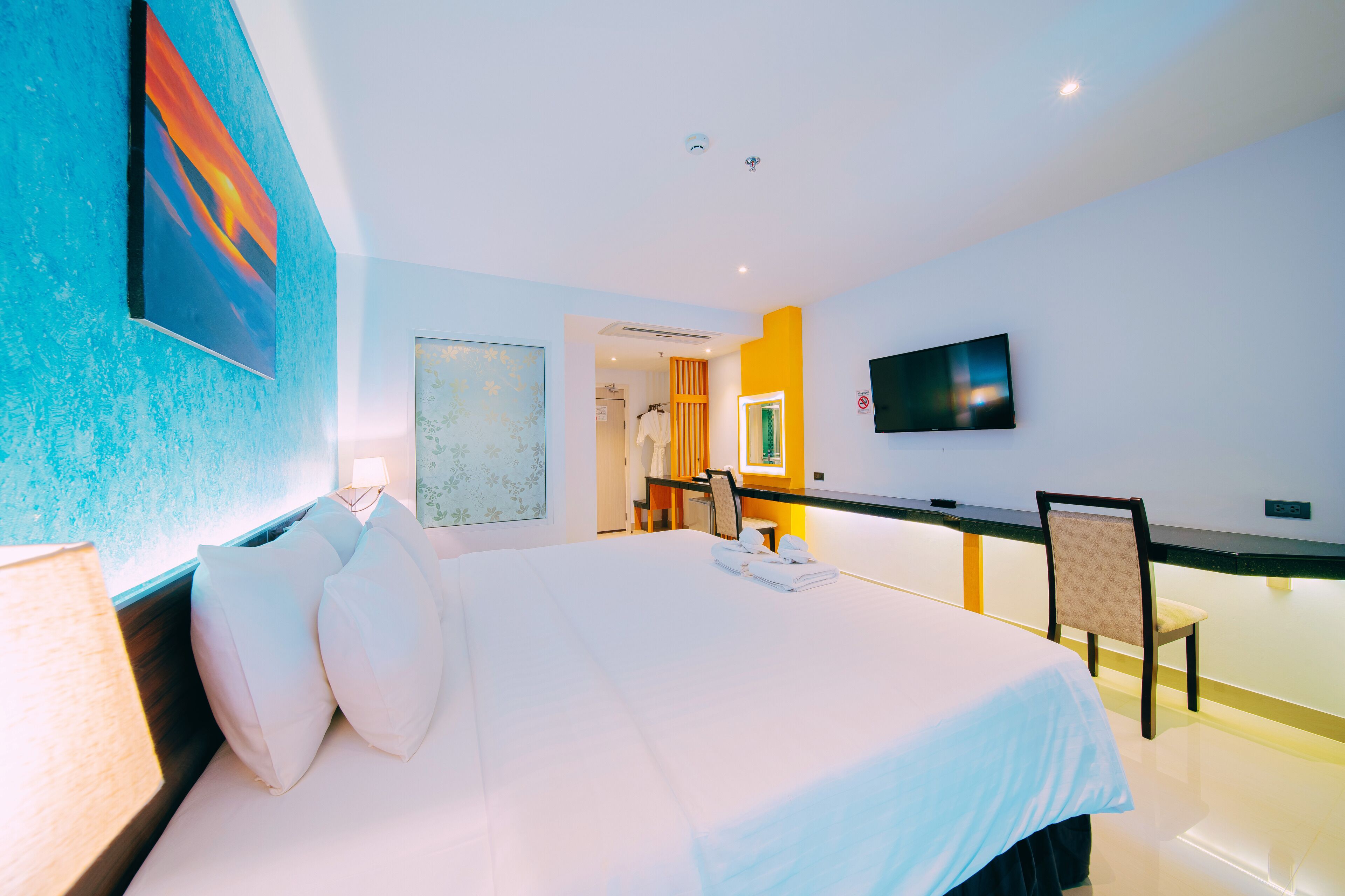 Une chambre d’hôtel moderne, dotée d’un grand lit, d’un bureau, d’une chaise, d’une télévision et d’une salle de bain visible à travers une porte ouverte.