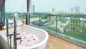 A modern bathroom with a freestanding bathtub, a glass-enclosed shower, and a view of a cityscape through large windows. - Royal Prince Resort Pattaya (Pattaya)