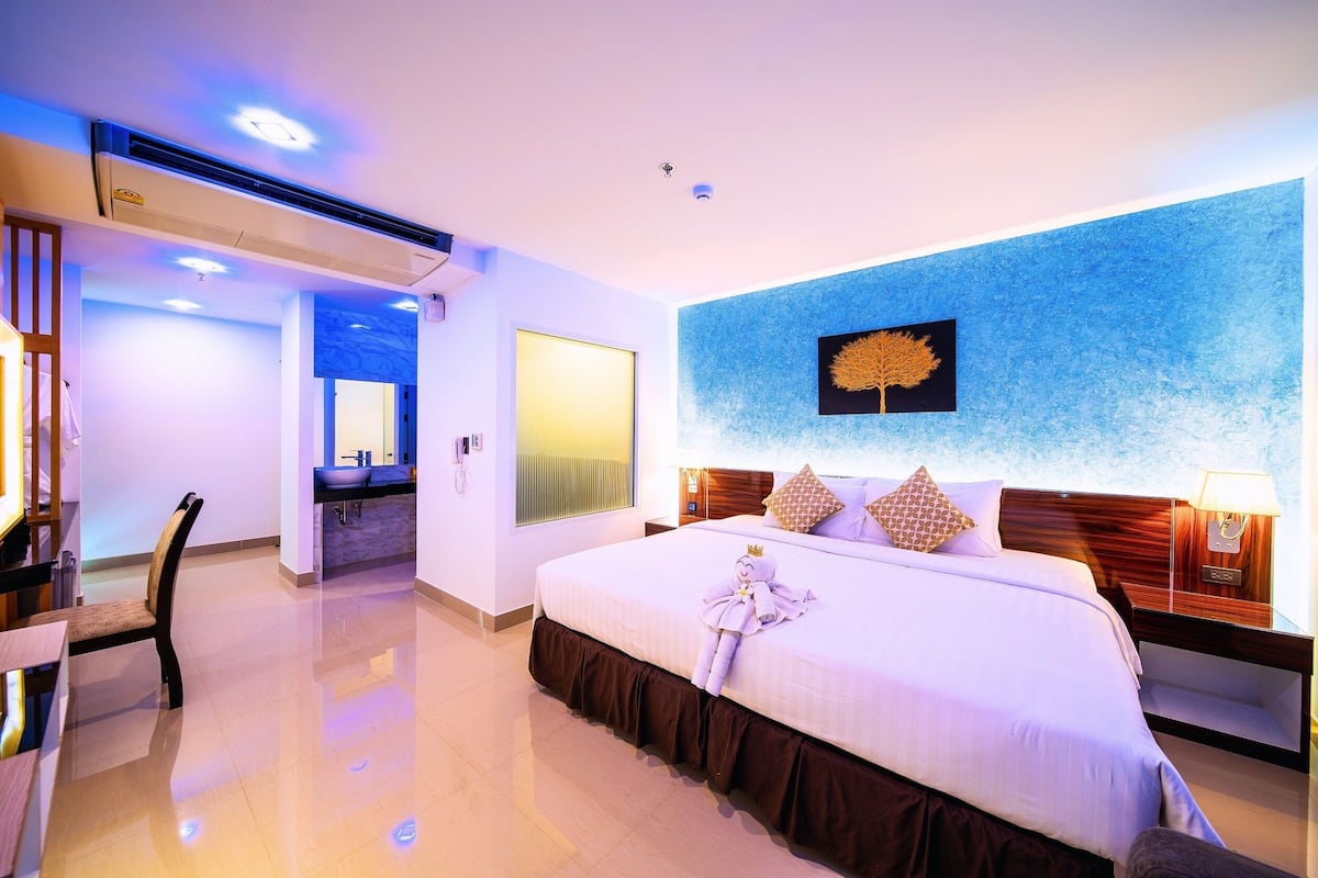 Ein Hotelzimmer mit einem großen Bett, einem Nachttisch mit Lampe, einem Wand-Fernseher und einem Deckenventilator.
